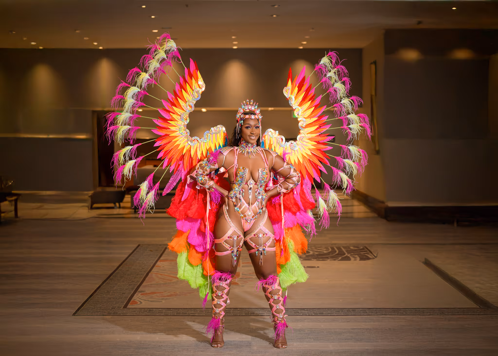 Woman wearing an elaborate carnival costume with colorful wings and feathers in pink, yellow, orange, and green.