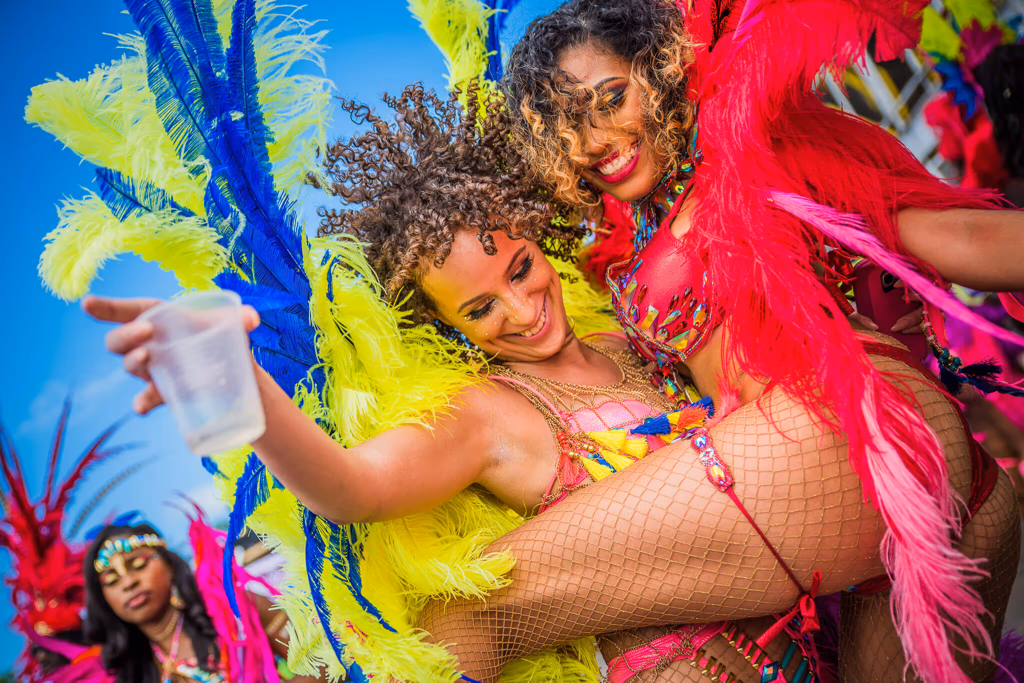 Two women dressed in vibrant carnival costumes with colorful feathers, smiling and dancing joyfully.
