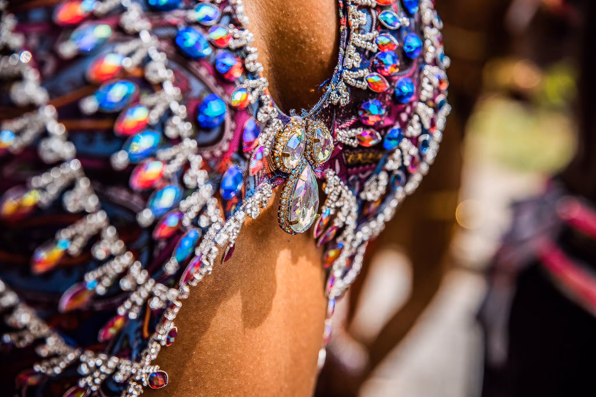 Close-up of a vibrant carnival costume adorned with colorful gemstones and sparkling rhinestones on tanned skin.