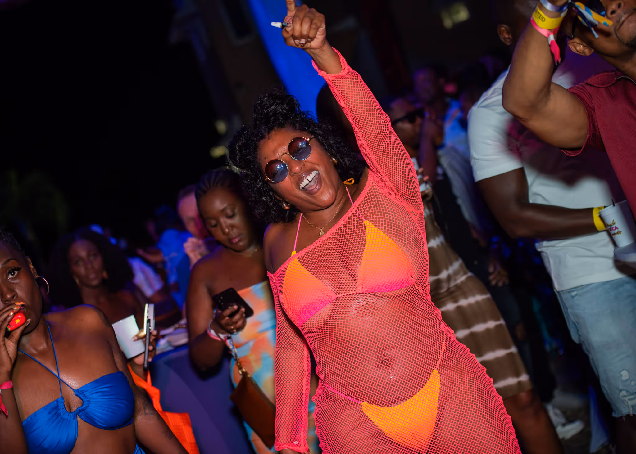 Woman in pink mesh top and neon bikini dancing energetically at a nighttime party.