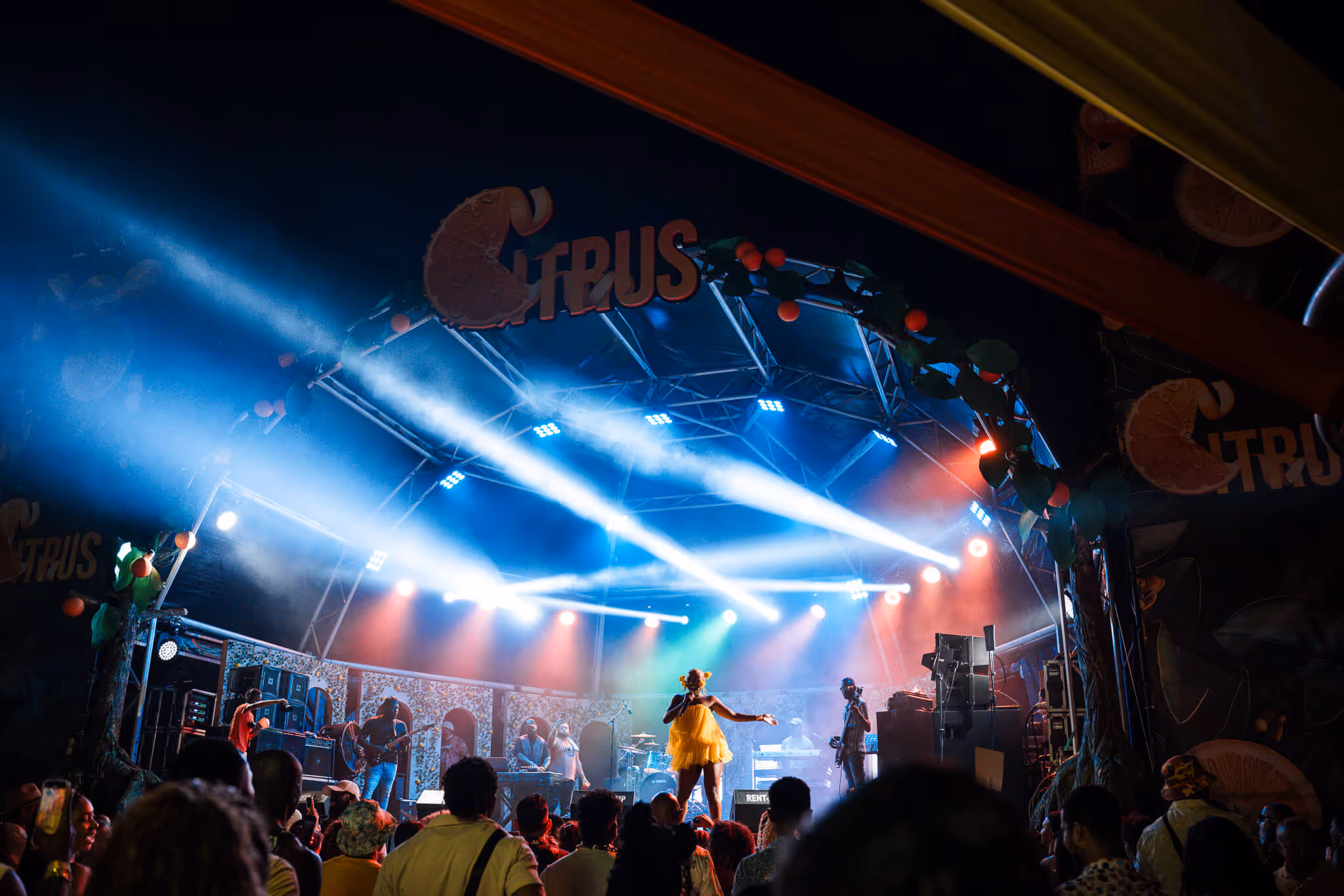 Live music performance on a brightly lit stage with colorful spotlights and a crowd watching.