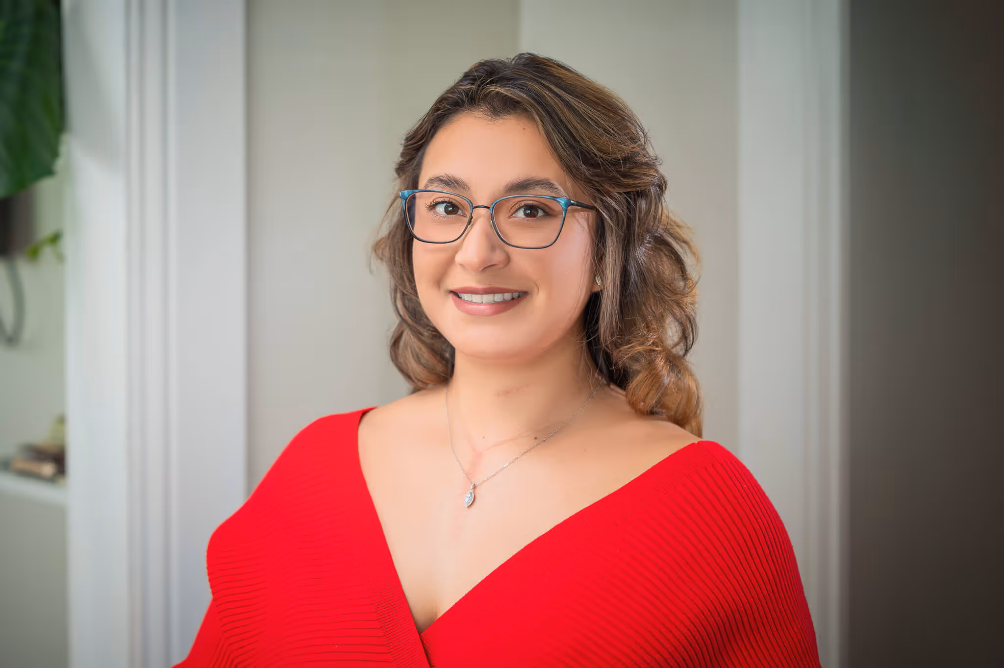 Smiling woman with glasses wearing a red off-shoulder top in a bright indoor setting.