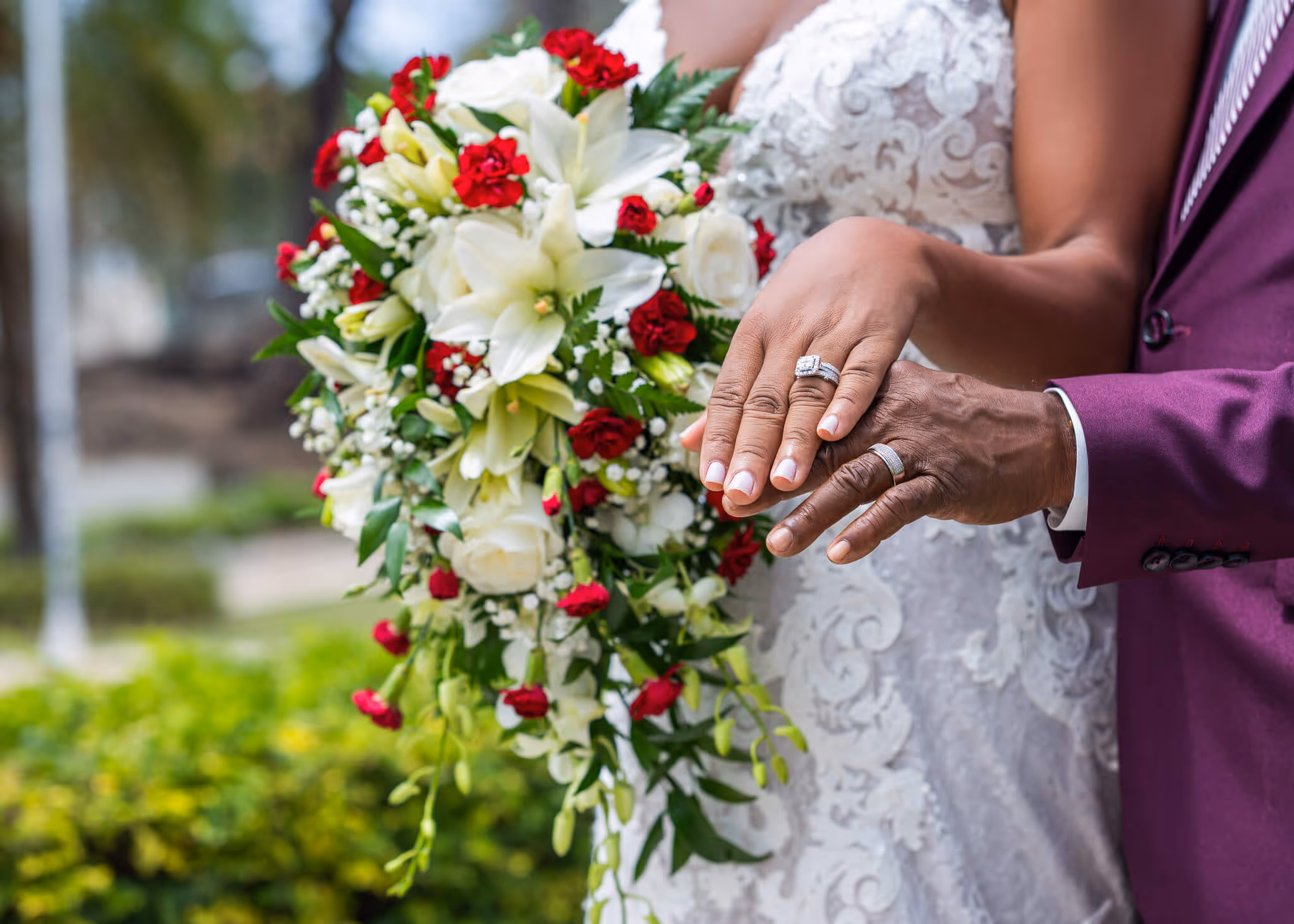 Bride and groom showing wedding rings with bride holding a bouquet of white lilies and red roses.